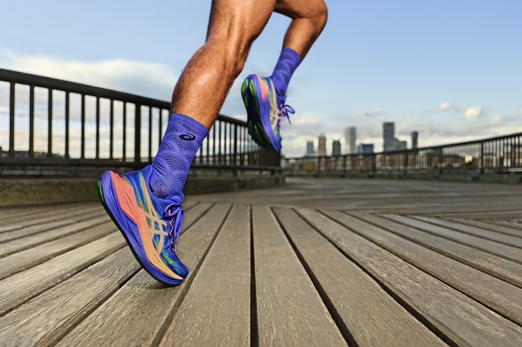 Runner wearing purple socks and vibrant blue-pink Superblast shoes sprinting along a wooden boardwalk with a city skyline in the background. - Totalsports