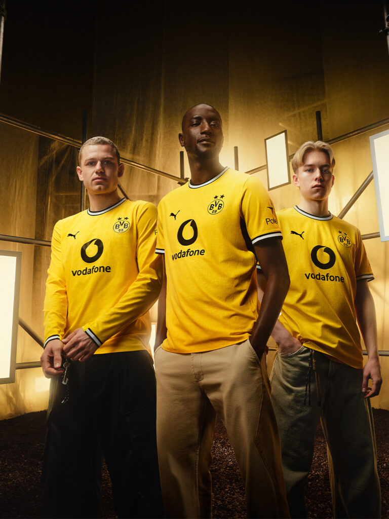 Yellow BVB home matchwear jerseys worn by football players with Vodafone branding, standing together in a dim indoor hallway - Totalsports