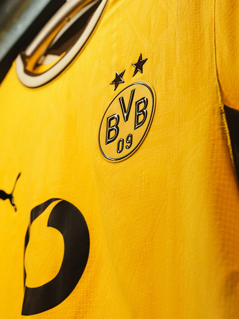 Close-up of a BVB 09 home matchwear jersey in bright yellow with black Puma logo and embroidered club crest for Borussia Dortmund fans - Totalsports
