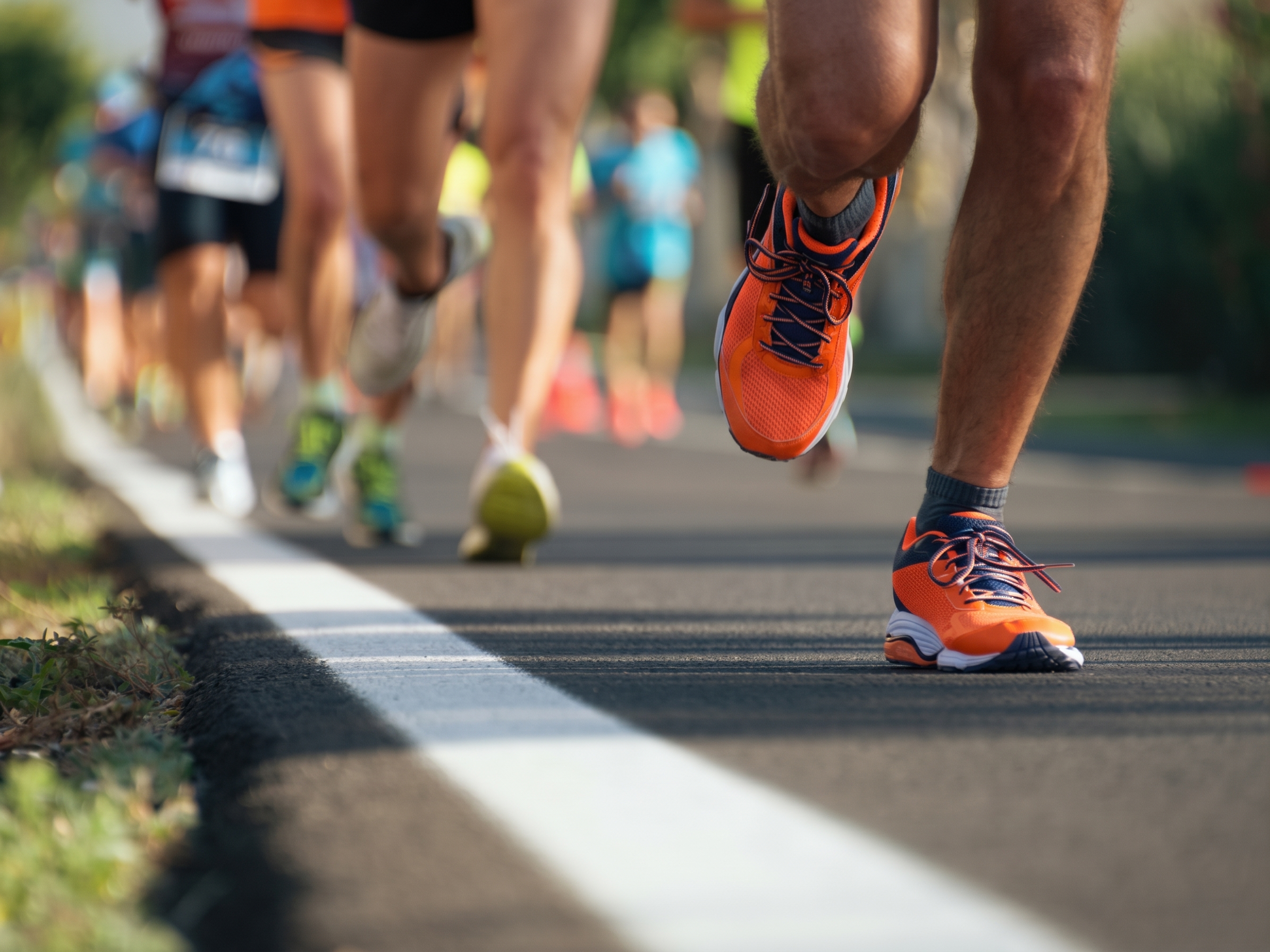 Runners stride across a road during The Slave Route Challenge, with orange racing shoes leading the pack along the course. - Totalsports