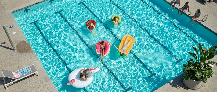 Participants float in a turquoise swimming pool with colorful rings and inflatable toys during a sunny day outdoors. - Totalsports