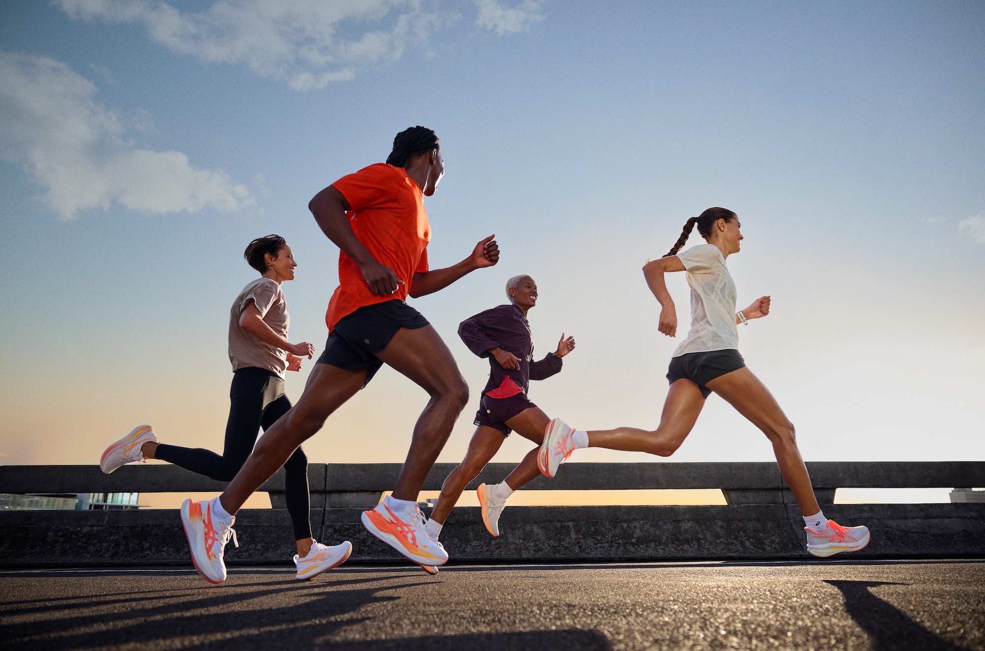 Four runners stride across a bridge at sunrise in ASICS RISE & SHINE collection campaign imagery - Totalsports